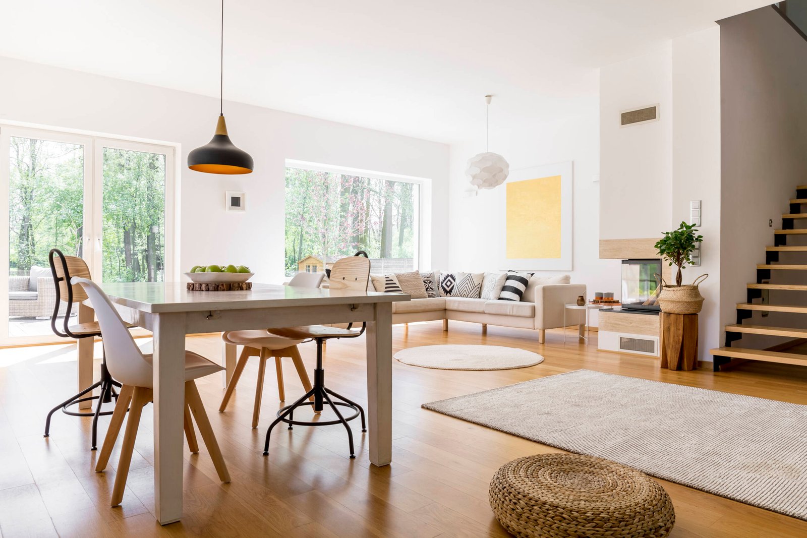 Black designed lamp above table Black designed lamp above dining table in spacious living room with braided pouf on wooden floor
