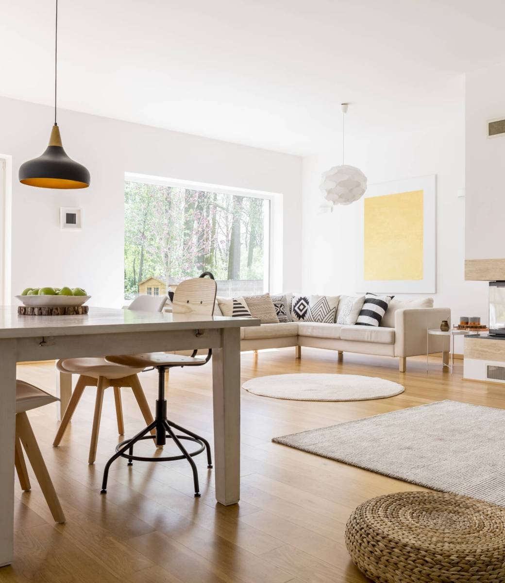 Black designed lamp above dining table in spacious living room with braided pouf on wooden floor