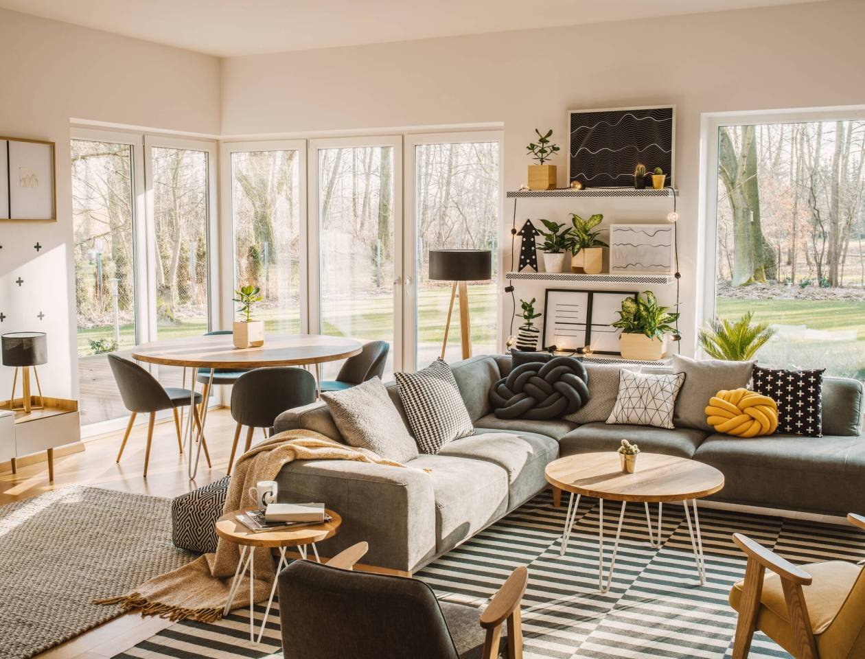 Wooden, round dining table in the corner of an open space living room interior with nordic furniture and decor